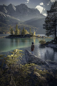 Rear view of man standing on rock in lake against mountains