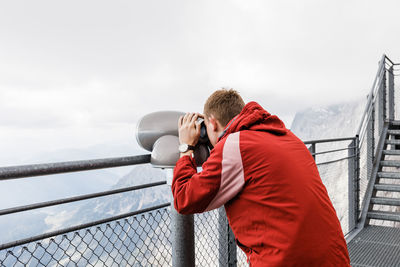 Young blond man looks at mountain views in binoculars from observation