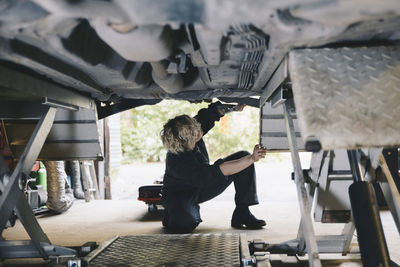 Female mechanic examining under car at auto repair shop