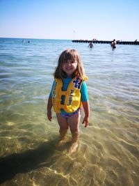 Portrait of cheerful girl standing in sea against clear sky