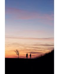 Silhouette men standing on shore against sky during sunset