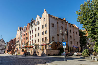 Road by buildings against clear blue sky