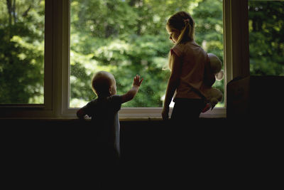 Girl looking at brother while standing by window