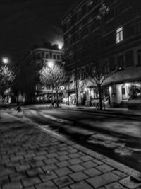 Illuminated street by buildings in city at night