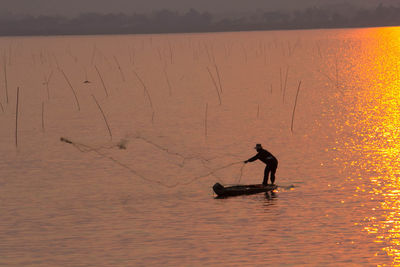 Silhouette man casting fishing net in lake during sunset