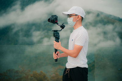 Young man holding a gimbal with a digital camera on a foggy mountain