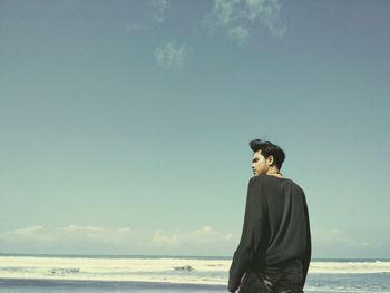Rear view of young man standing at beach against sky