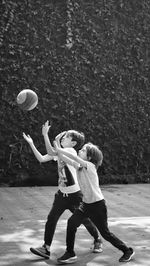 Siblings playing basketball on footpath