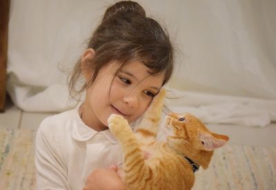 Close-up of cute girl with ginger cat sitting at home