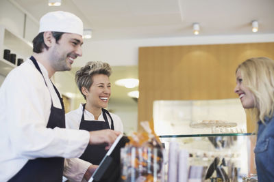 Happy worker attending female customer at cafe counter