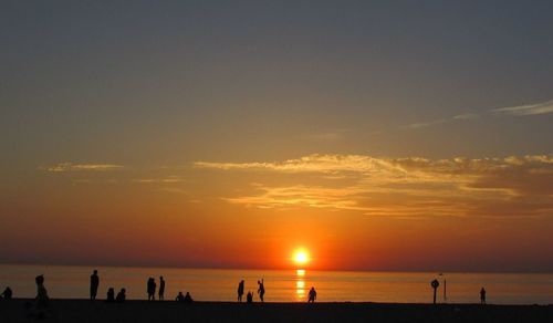 Silhouette people enjoying at beach against orange sky during sunset