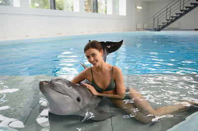 Portrait of smiling young woman with dolphin in swimming pool