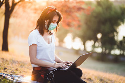 Young woman using mobile phone while sitting on field