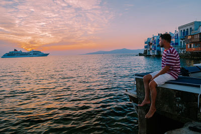 Woman sitting on sea against sky during sunset