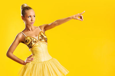 Beautiful ballerina pointing away against yellow background