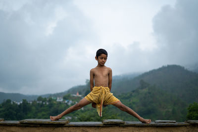 A young indian cute kid doing yoga in the mountains,wearing a dhoti