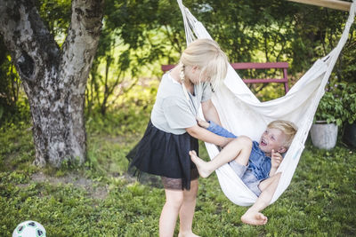 Playful sister tickling brother swinging in backyard