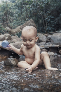 Full length of cute boy sitting in stream