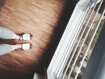 Low section of woman standing on hardwood floor by window at home