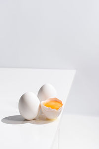 High angle of whole and broken egg with yolk in shell placed on edge of table on white background in studio