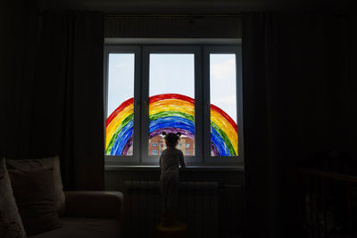 Little girl on background of painting rainbow on window. kids leisure at home. 