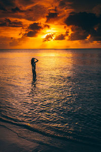 Woman wearing bikini while standing in sea during sunset