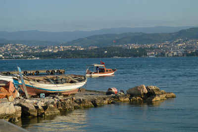 Boats moored on sea by mountains against clear sky