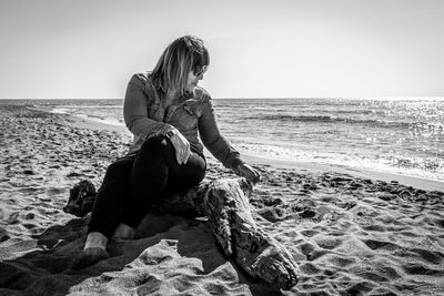 Man sitting on shore at beach against sky