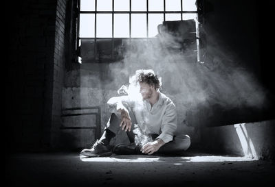 Man smoking while sitting on floor against window