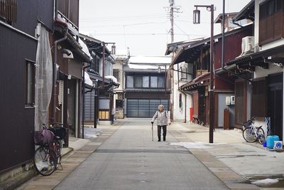 Rear view of man walking on street amidst buildings