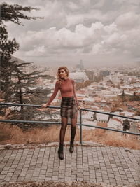 Full length of young woman standing against sky in city