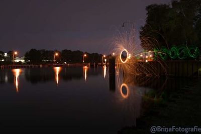 Illuminated trees by lake against sky at night