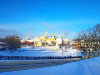 Snow covered trees and buildings against blue sky