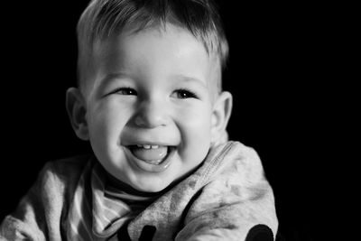 Close-up portrait of smiling boy against black background