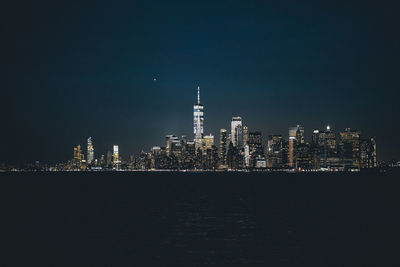 Illuminated buildings at waterfront against clear sky at night