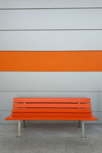 Empty orange bench by wall