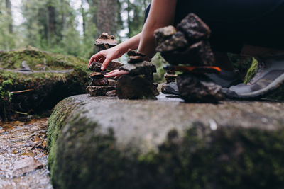 Midsection of woman sitting on rock in forest stacking stones