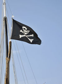 Low angle view of pirate flag against blue sky