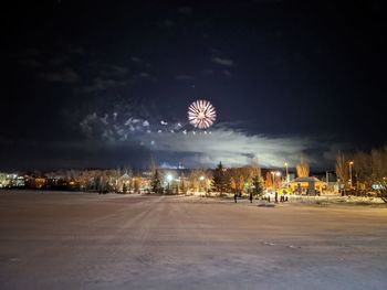 Firework display over illuminated city against sky at night