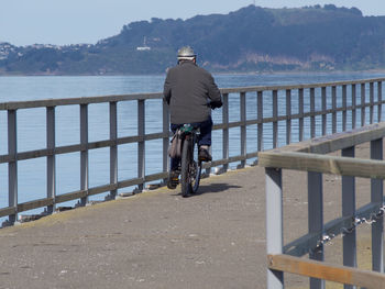 Rear view of man on bicycle by river