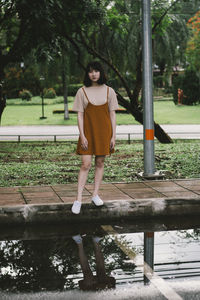 Full length portrait of young woman standing on sidewalk by puddle