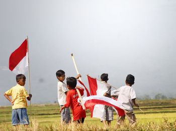 Boys holding flags while standing on grassy field against sky