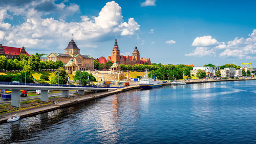 View of buildings by river against cloudy sky