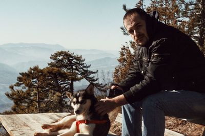 Portrait of man with dog sitting against trees