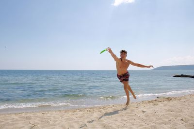 Full length of shirtless boy on beach against sky