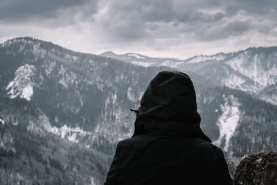 Rear view of person in black winter jacket looking at snowcapped mountains in winter