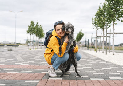 Smiling young woman in yellow hoodie hugging her fluffy shaggy gray dog, pet love and walking dog,l