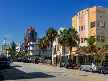 Cars on road by buildings against blue sky