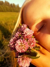 Cropped image of girl holding pink flowers on field during sunset