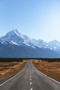 Empty road leading towards snowcapped mountains against sky